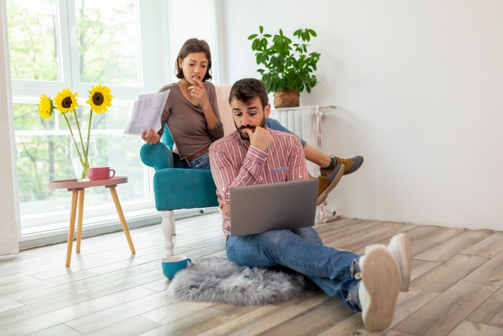 Young couple managing their finances, reviewing bank accounts on a laptop computer, calculating bank loans and debts, and make payments online; Thinking of refinancing to pay less
