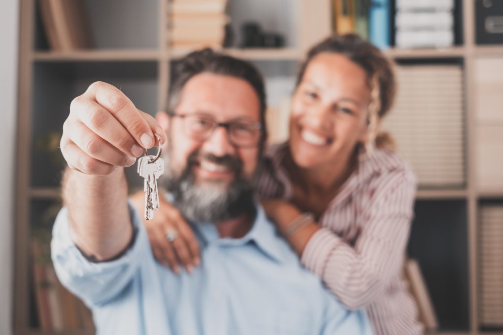 Focus on keys, held by excited young spouses homeowners. Happy married family couple celebrating moving in new house home , demonstrating keys, standing in apartment, real estate mortgage concept. Settlement day done