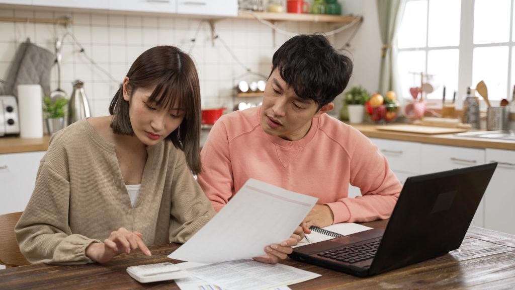 married couple calculating budget on calculator in dining room at home. the surprised man holding his head worrying about lack of money to pay the home loan