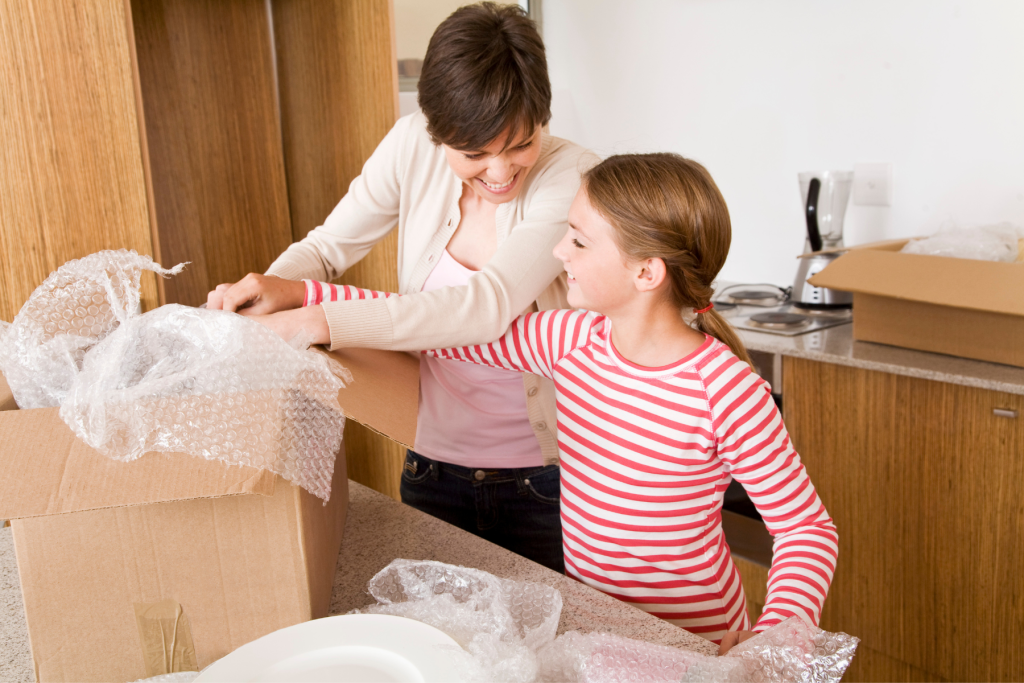 Family Home Guarantee Daughter helping her single mom unpack the plates from the moving boxes 