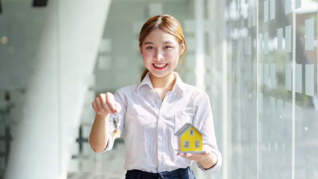Young woman in her 20s holding a miniature house and the key of her investment property
