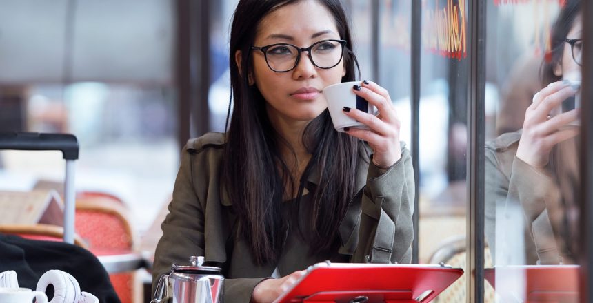 Shot of beautiful young asian woman using her digital tablet while drinking coffee in coffee shop.