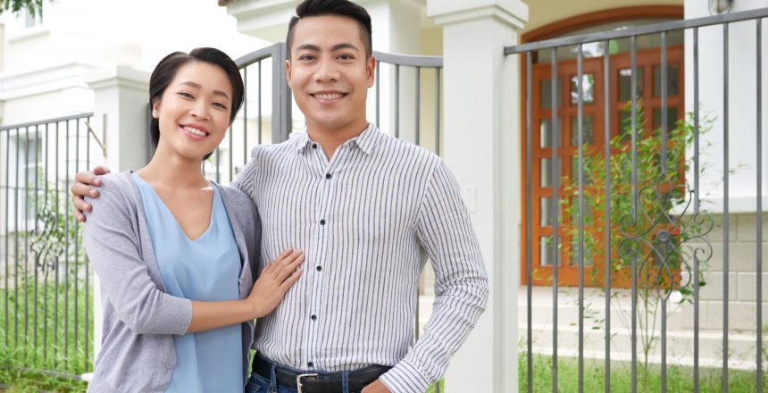 Happy young Vietnamese couple standing in front of their new house